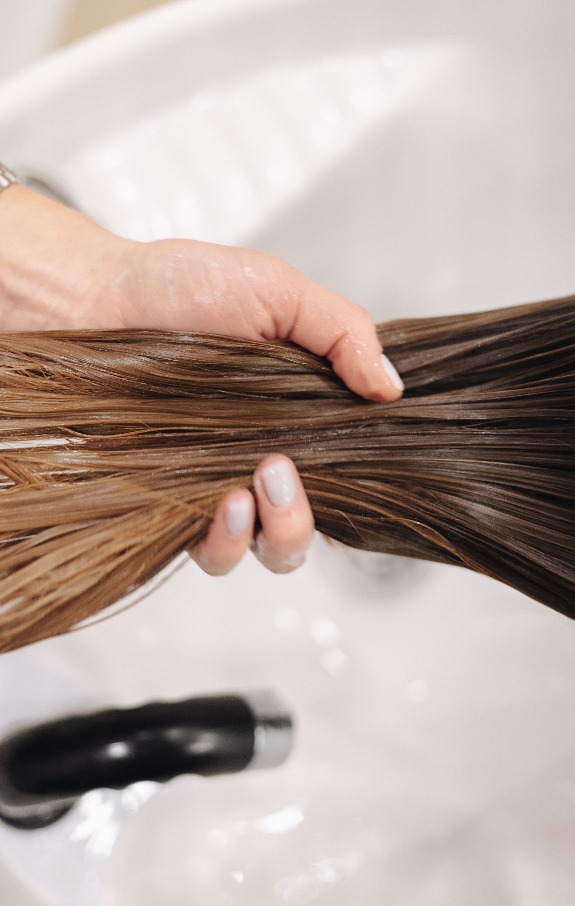 Close-up of a hand holding wet hair in a salon sink, showcasing hair treatment.